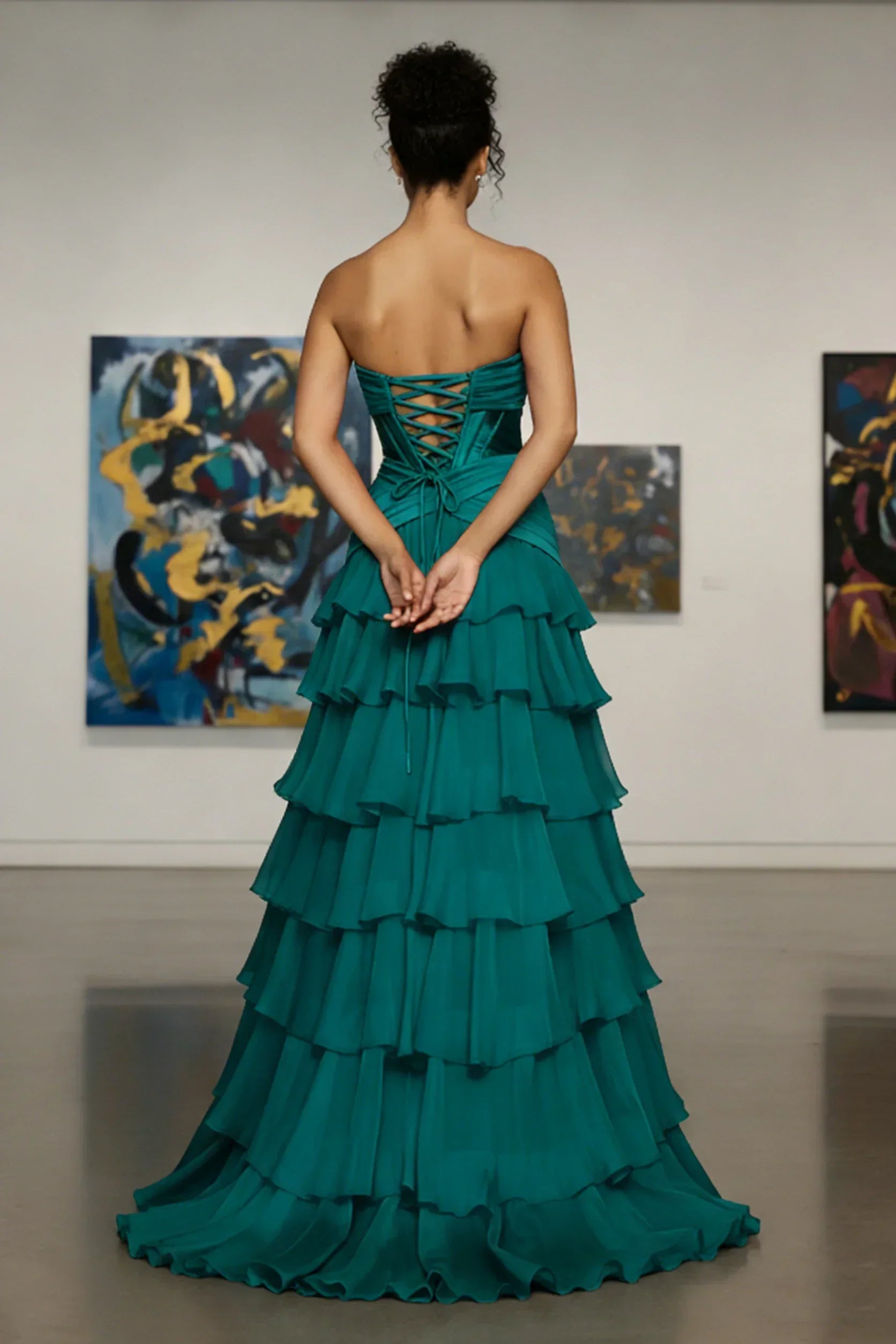 Woman in a strapless teal tiered evening gown with lace-up back standing in art gallery
