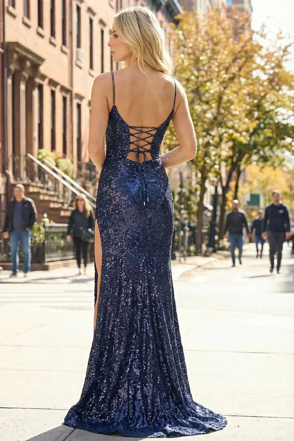 Back view of Sevoba dark blue sequin evening gown showing a lace-up corset back and fitted silhouette, city street background. 