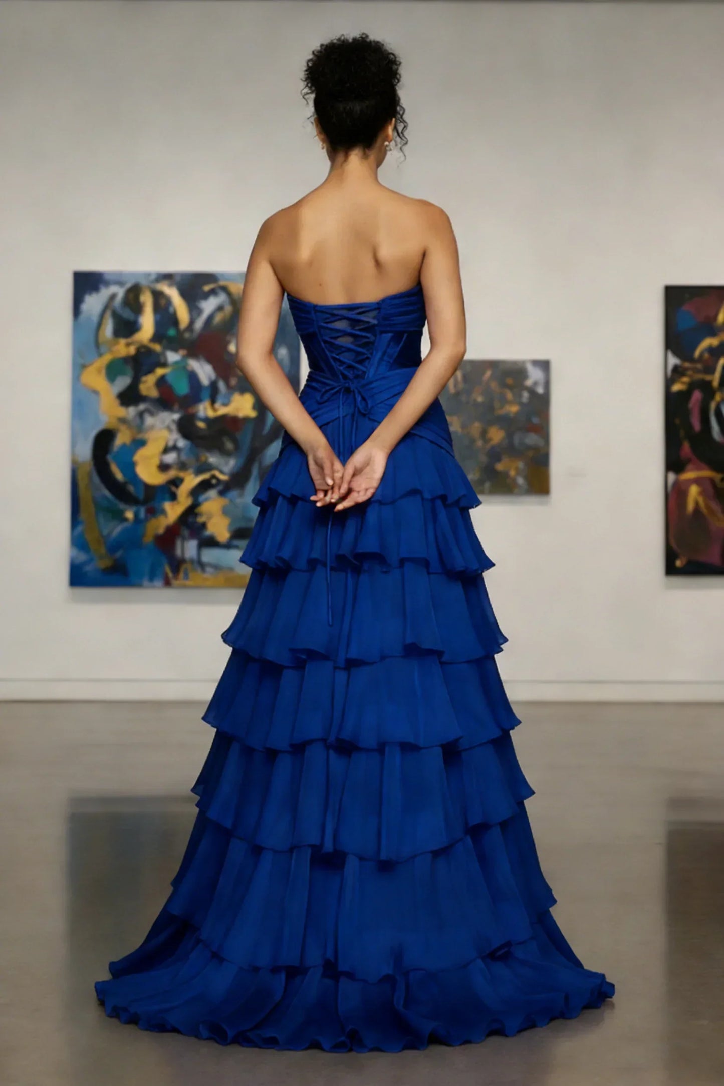 Woman in strapless royal blue tiered evening gown stands in modern art gallery