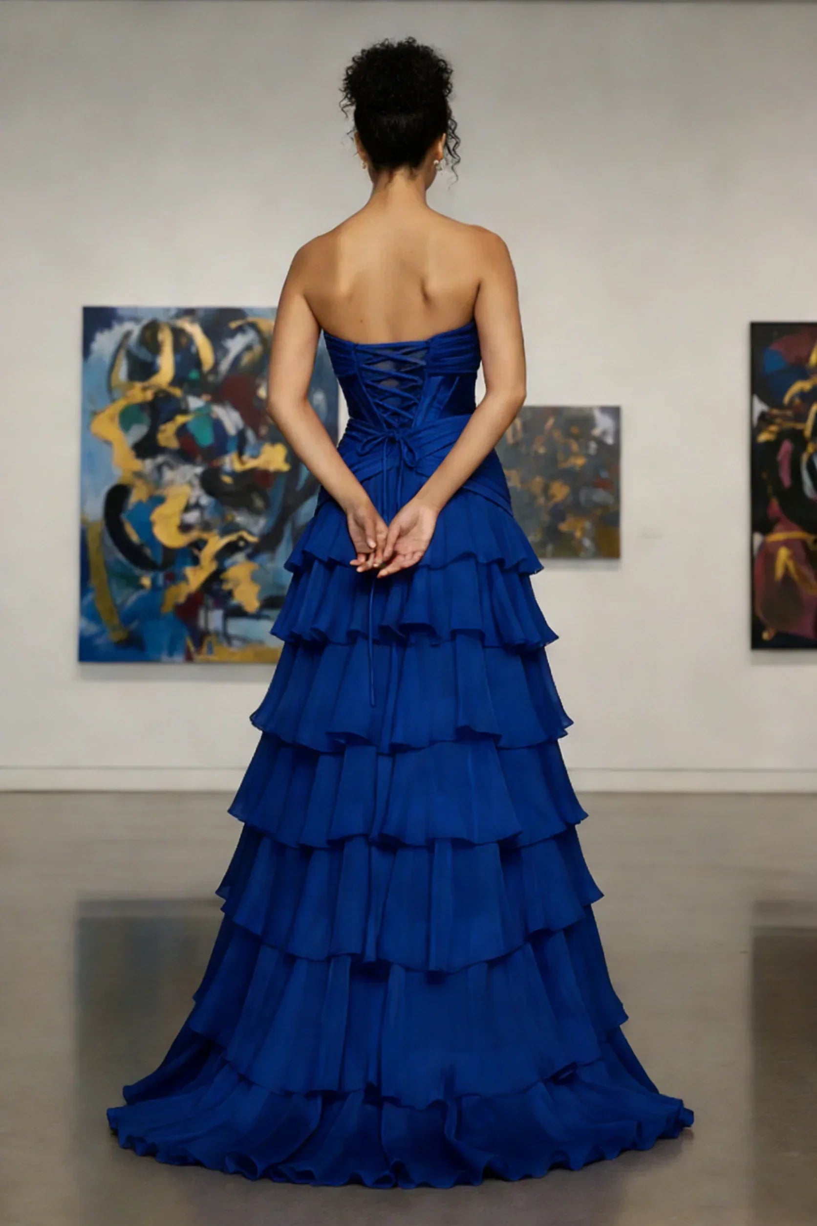 Woman in strapless royal blue tiered evening gown stands in modern art gallery