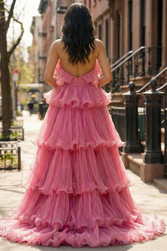 Back view of Sevoba pink maximalist evening gown showing layers of cascading pleated ruffles and a floor-length silhouette, street background