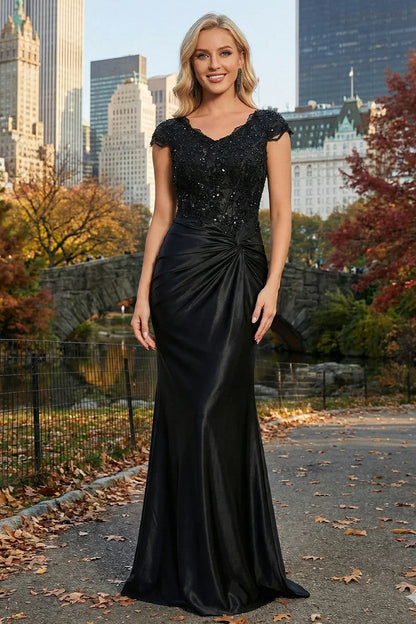 Sevoba black satin mermaid prom dress with beaded lace cap sleeves and flattering twist knot waist, front view in park setting
