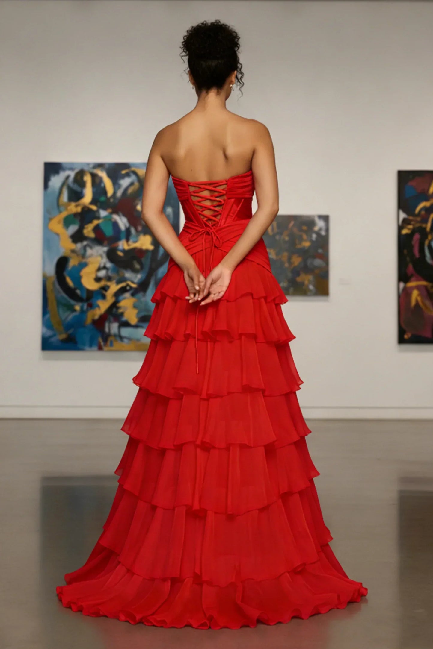 Woman in a strapless red tiered evening gown with lace-up back, standing in an art gallery.