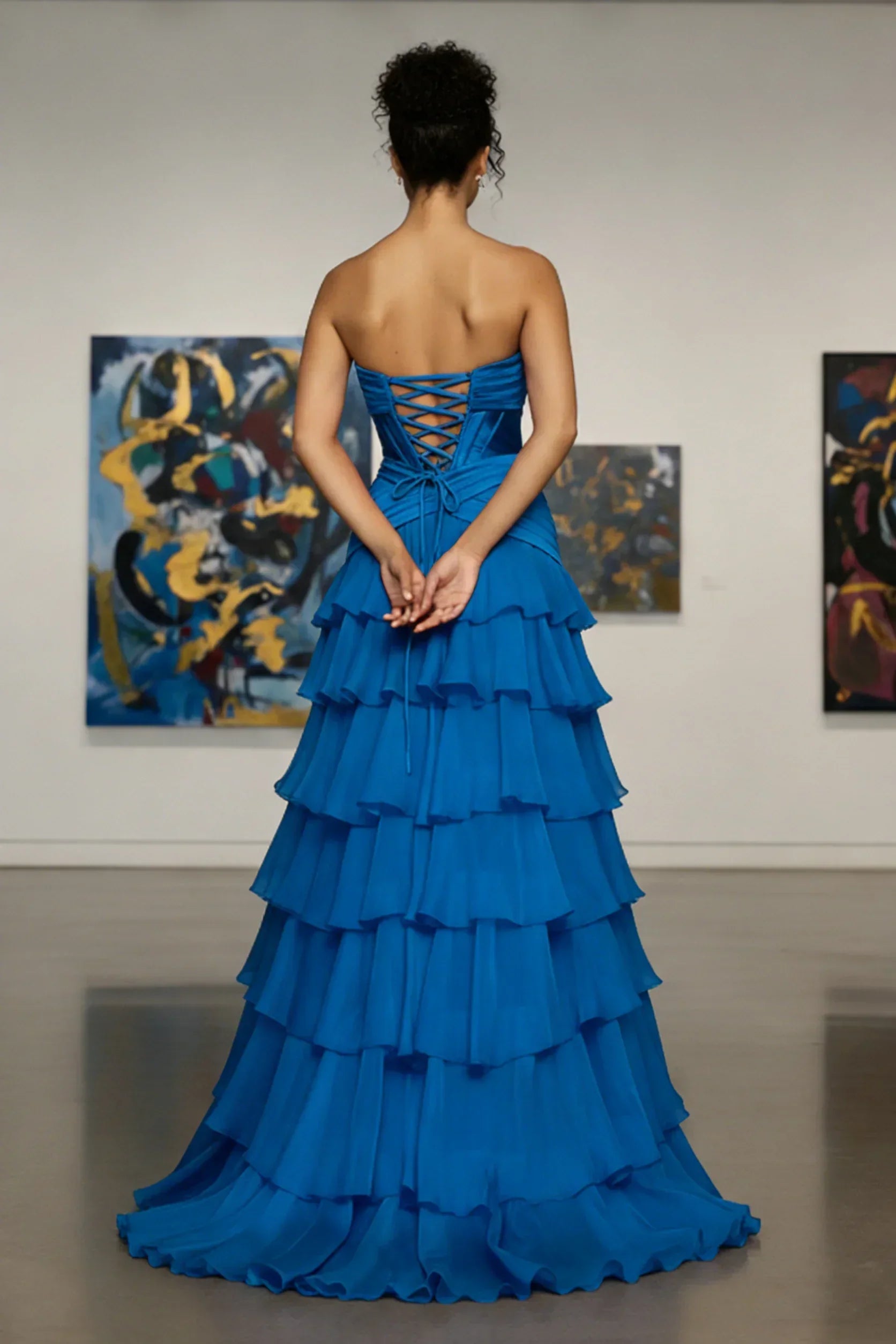 Woman wearing strapless tiered blue evening gown with lace-up back in art gallery