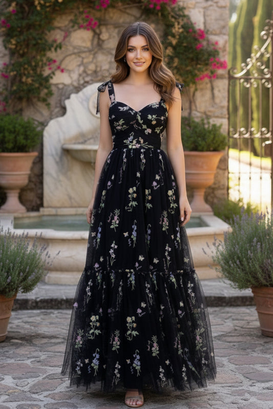 Sevoba black sweetheart embroidered floral tulle A-line prom dress with bow straps and tiered skirt, front view in courtyard fountain setting
