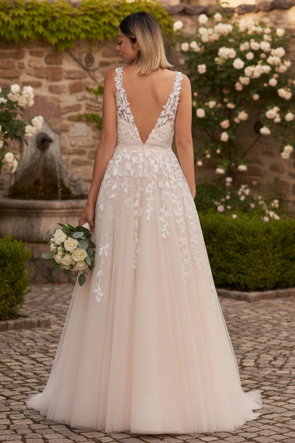 Sevoba ivory applique lace tulle A-line prom dress with low V back and sweep train, back view in garden courtyard