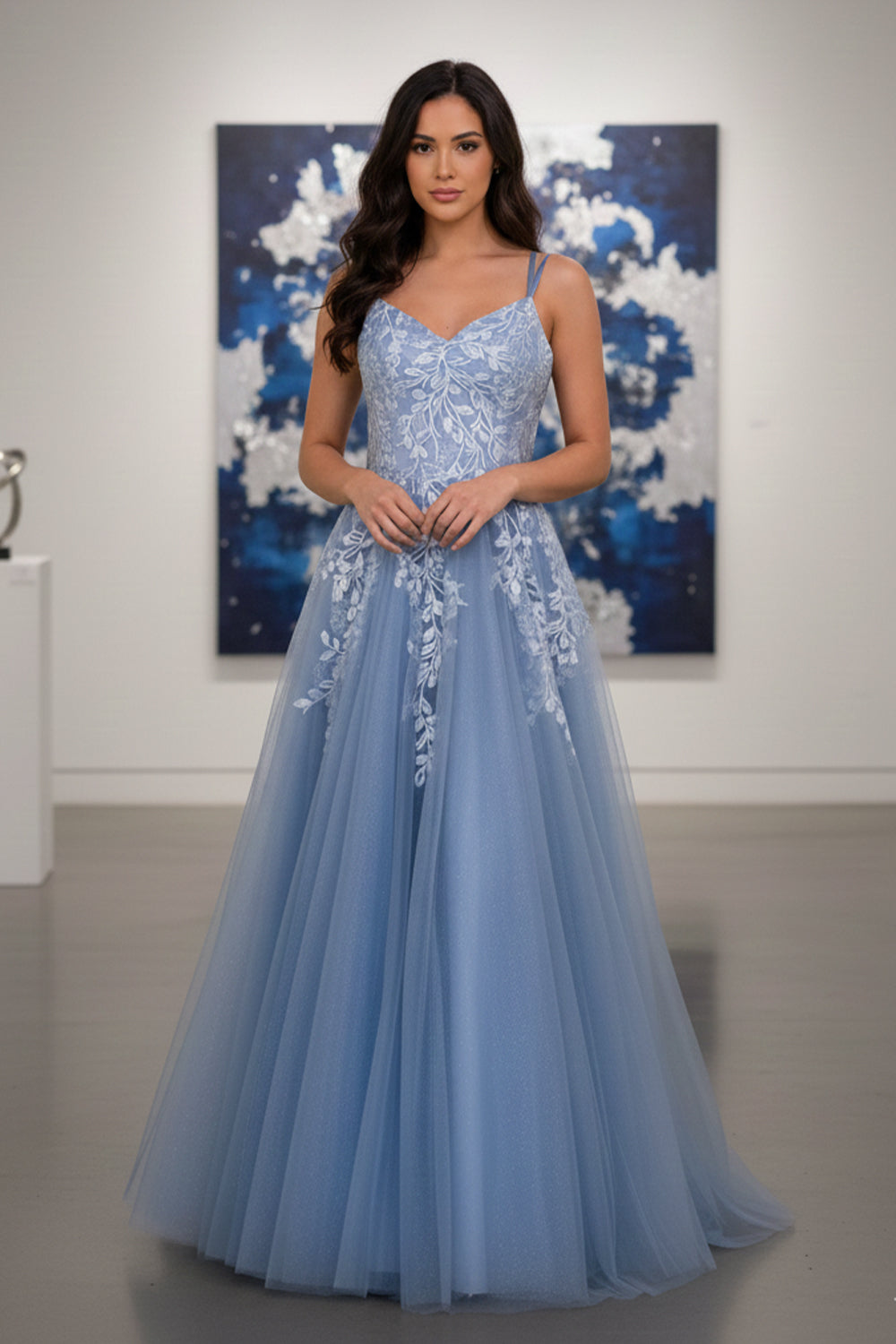 Sevoba dusty blue glitter tulle A-line prom dress featuring white leaf lace appliqués and double spaghetti straps, front view in art gallery setting