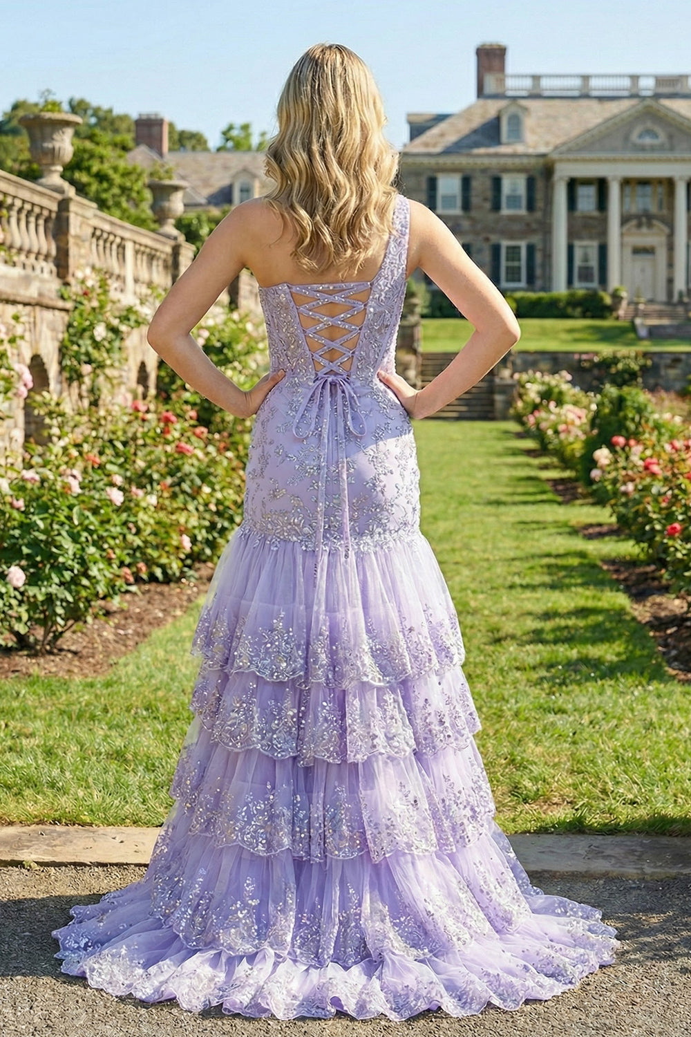 Back view of Sevoba lilac sequin evening gown showing a lace-up corset back and tiered ruffle mermaid skirt, outdoor garden background.