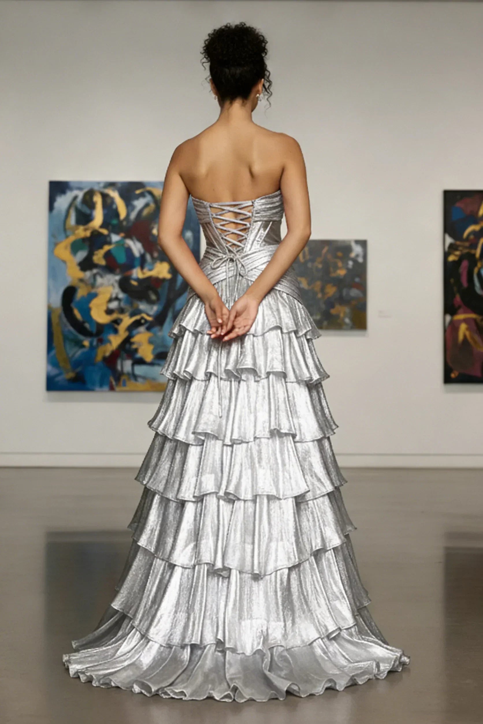 Woman in strapless silver tiered evening gown with lace-up back, standing in art gallery