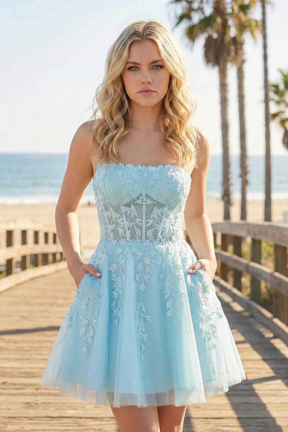 Woman in light blue A-line tulle lace homecoming dress with floral appliqué on boardwalk by the beach