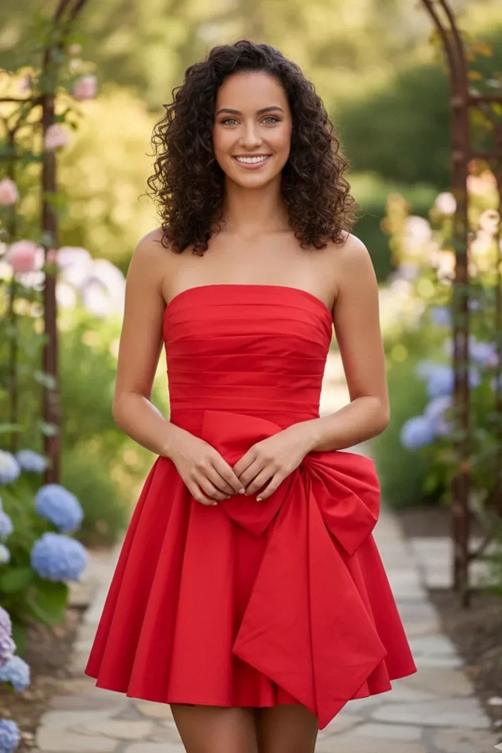 Woman in a red strapless A-line mini homecoming dress with large bow, standing outdoors