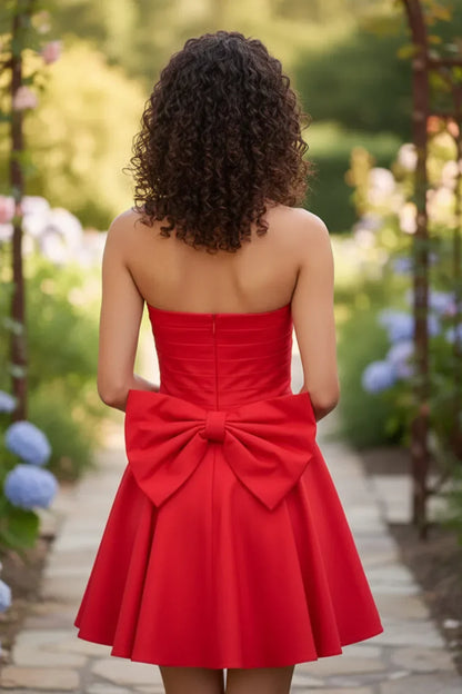Back view of strapless red mini A-line homecoming dress with a large bow, outdoor garden