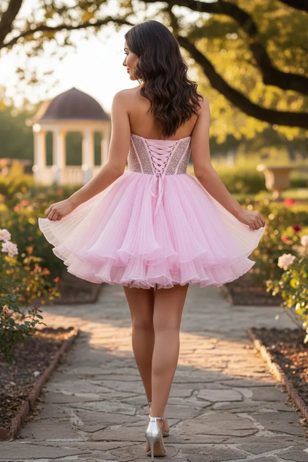 Woman in pink strapless ruffled short homecoming dress with corset back and layered skirt outdoors