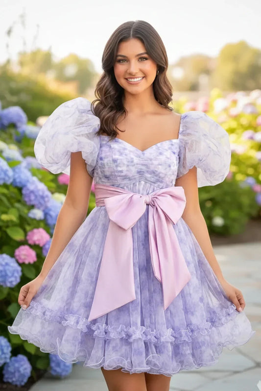 Lavender A-line homecoming dress with sweetheart neckline, puff sleeves, and pink bow, outdoors.