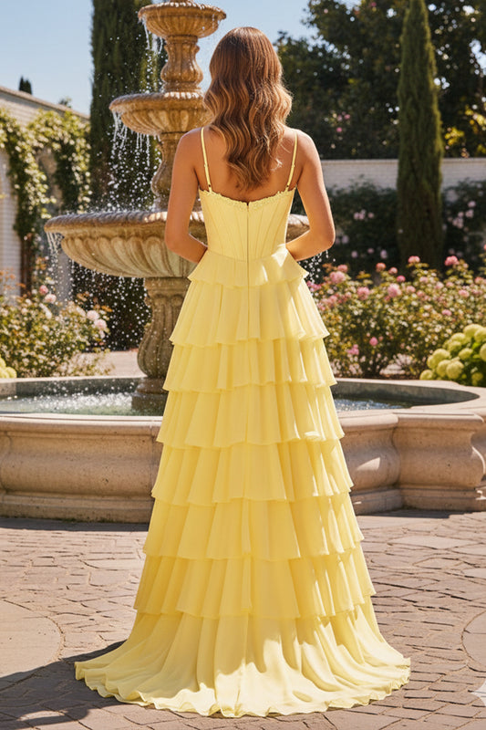 Back view of Sevoba yellow evening gown showing a zipper closure and voluminous layered ruffle skirt, garden fountain background