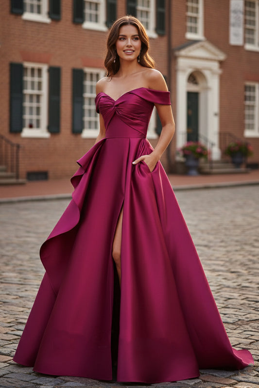 Sevoba magenta satin A-line prom dress featuring an off-the-shoulder twisted neckline, high leg slit, and pockets, front view in outdoor brick street setting