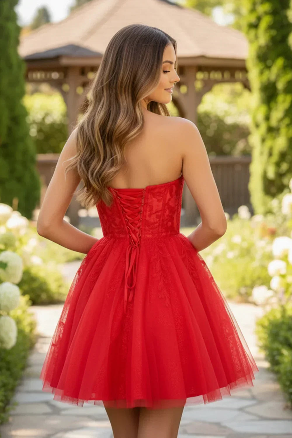 Woman in red A-line lace homecoming dress with corset back, standing in a garden