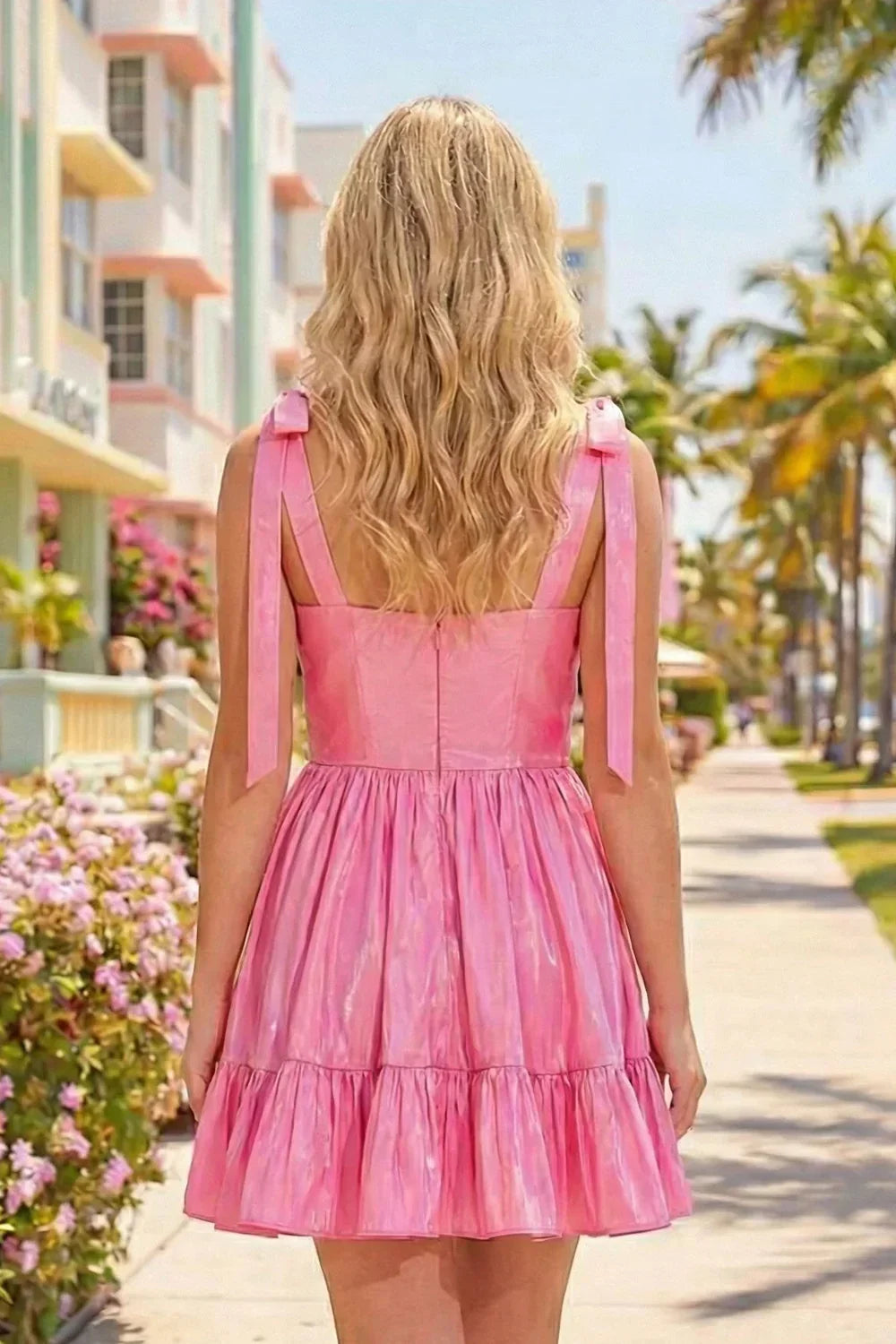 Back view of a blonde woman wearing a pink ruffled A-line taffeta homecoming dress with bow straps outdoors