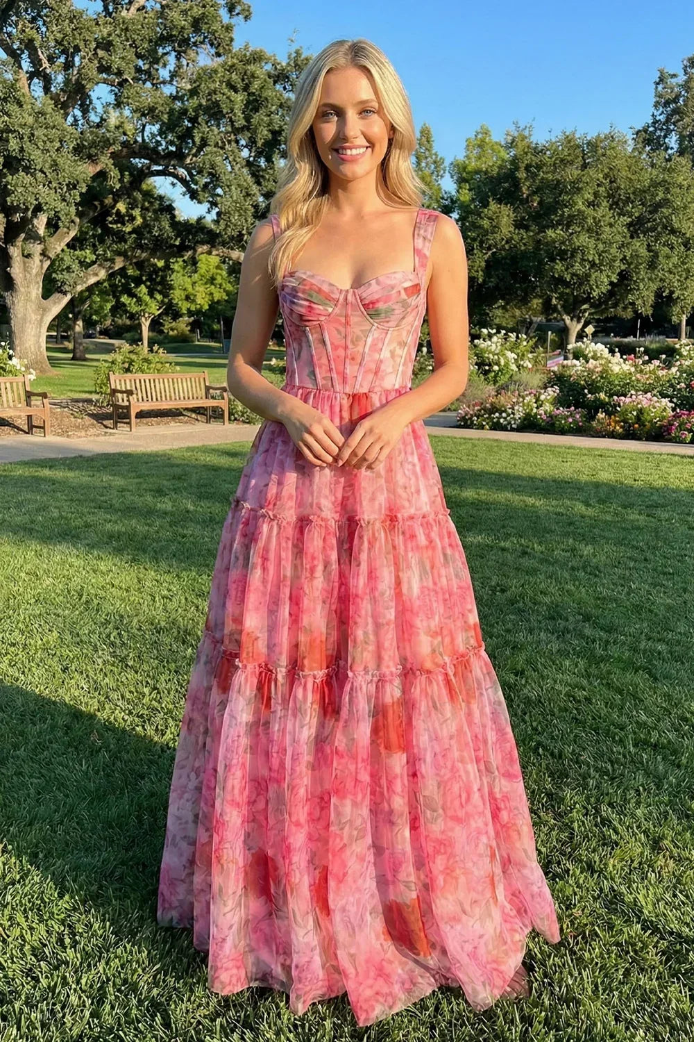 Woman in a pink floral A-line long prom dress standing in a sunny outdoor garden