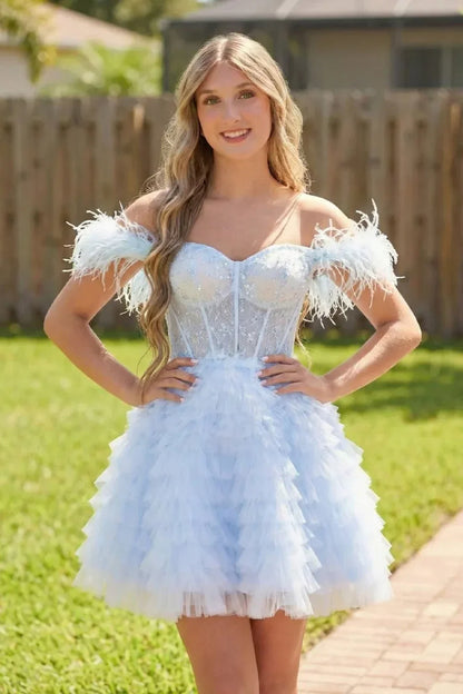 Woman wearing a light blue A-line off-the-shoulder homecoming dress with feathered sleeves and ruffled skirt, posing outdoors.