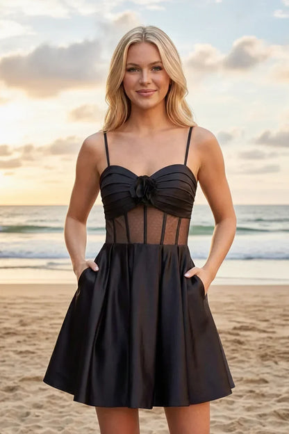 Woman in black satin A-line homecoming dress with illusion bodice and 3D flower, on beach