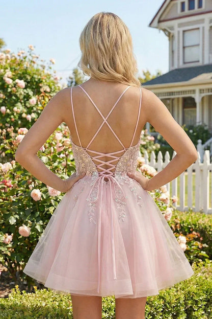 Back view of a short pink homecoming dress with lace-up straps and floral appliques in a garden.