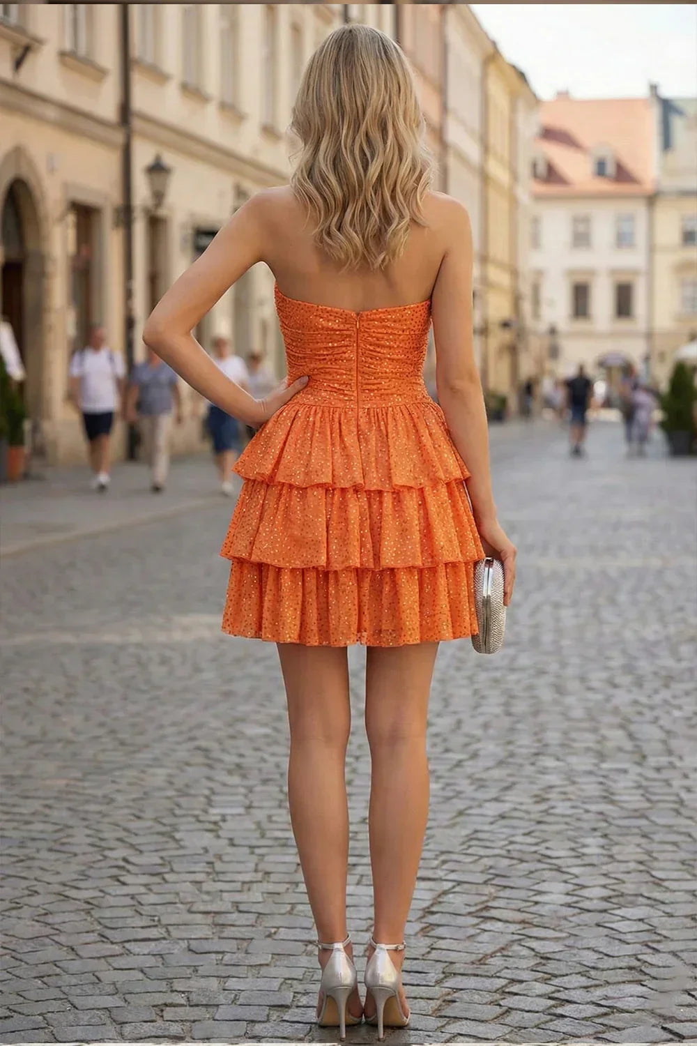 Woman in a strapless orange ruffled satin homecoming dress with beads, holding a clutch on a city street