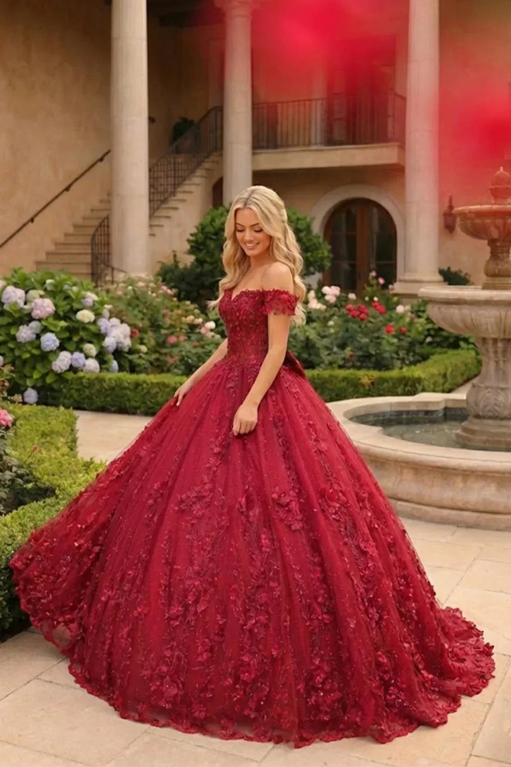 Woman in a red floral lace ball gown with off-shoulder sleeves in a garden courtyard