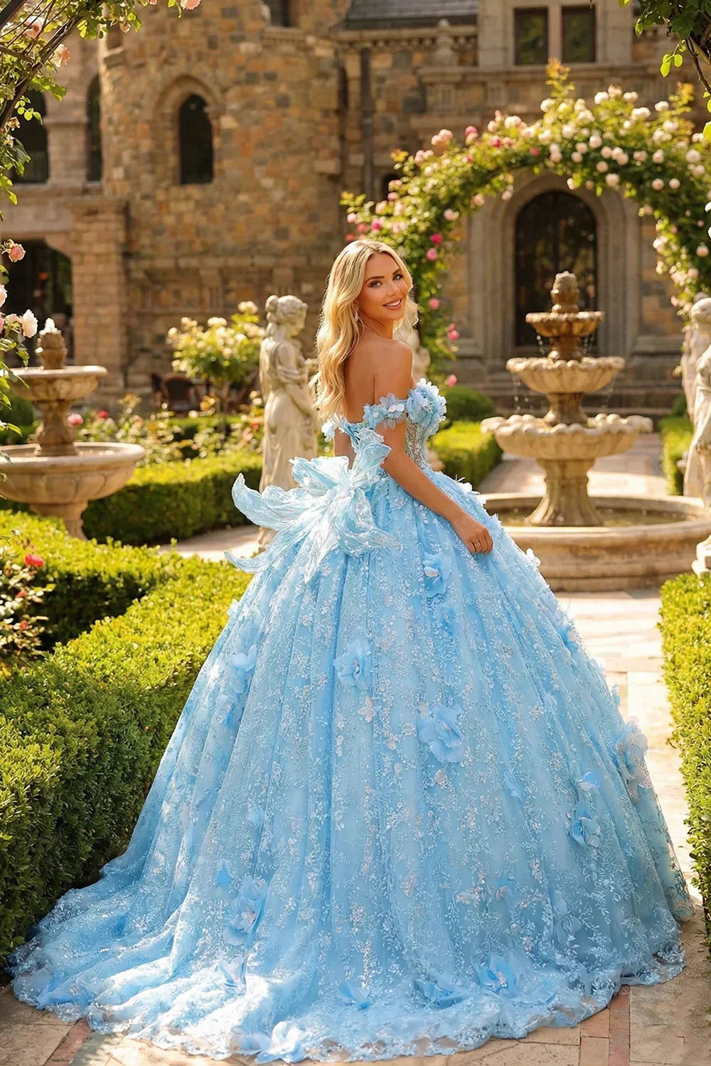 Woman in blue off-shoulder ball gown with 3D floral details, standing in a garden by a fountain