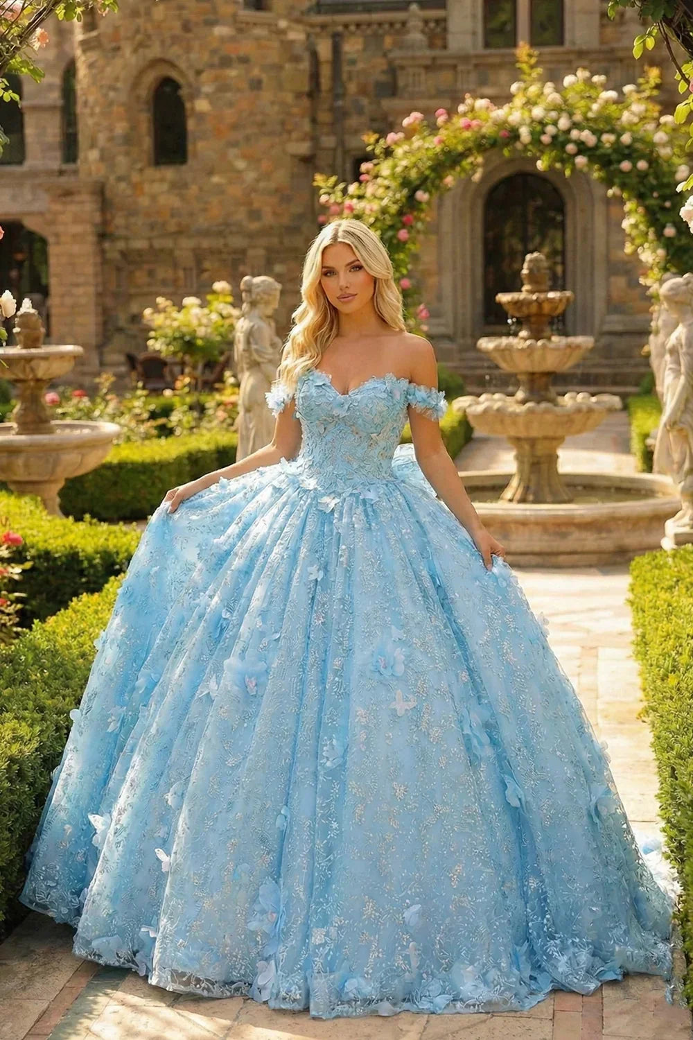 Woman in a blue off-shoulder ball gown with 3D floral accents posing in a garden setting