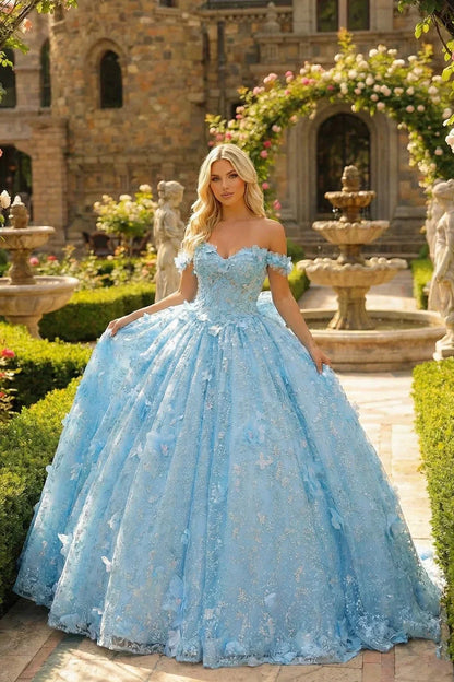 Woman in a blue off-shoulder ball gown with 3D floral accents posing in a garden setting