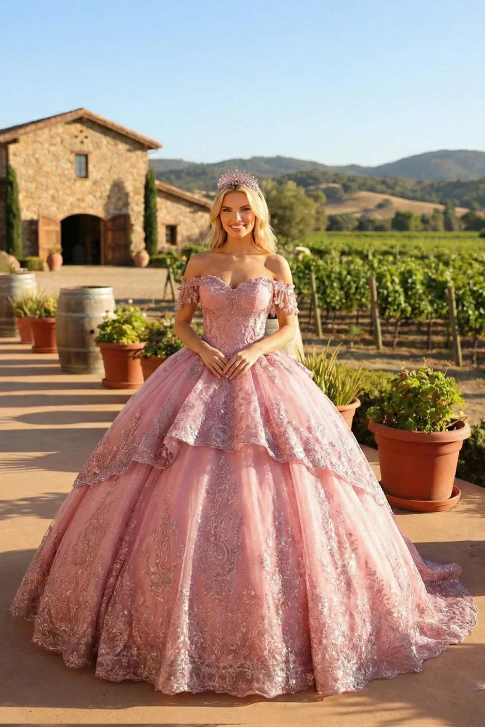 Woman in pink off-shoulder ball gown with floral appliqué and tiara outdoors by a vineyard