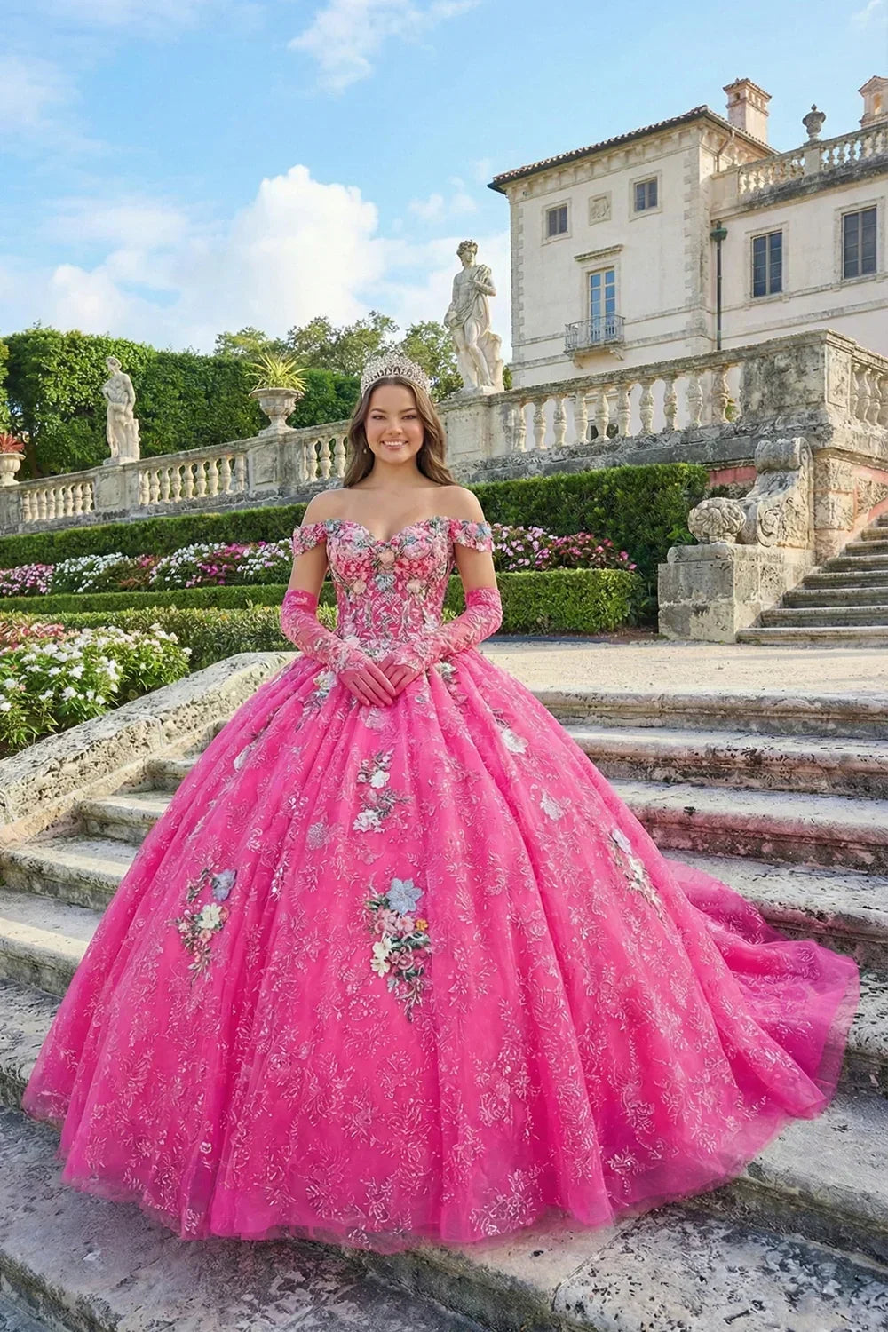Young woman in pink floral ball gown with off-shoulder sleeves and tiara, posing outdoors