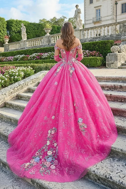 Woman in a pink ball gown with floral embroidery and cold shoulder sleeves outdoors