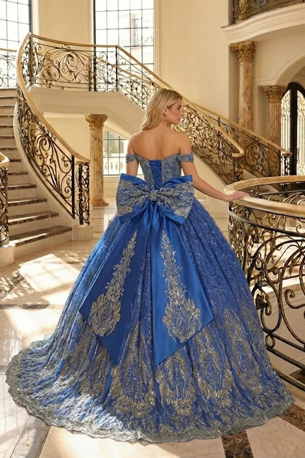Elegant blue off-the-shoulder ball gown with gold floral lace and large bow on staircase