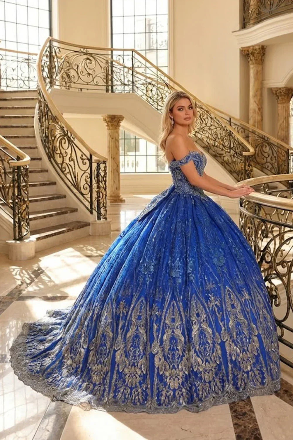 Woman in an elegant royal blue off-the-shoulder ball gown with floral lace detailing on a grand staircase.