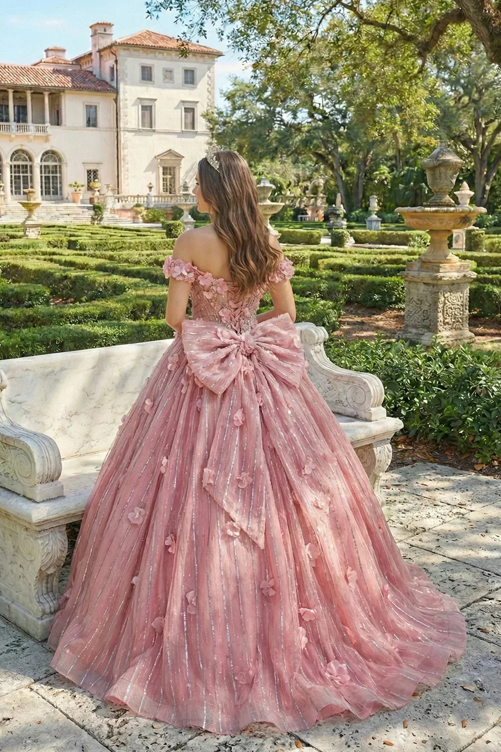 Woman in pink off-the-shoulder ball gown with 3D floral lace and large bow in a garden