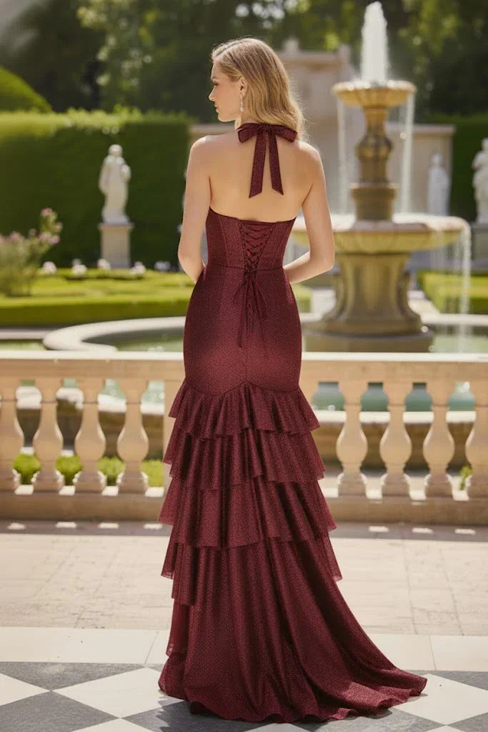 Woman in burgundy halter cowl neck tiered mermaid prom dress standing by fountain