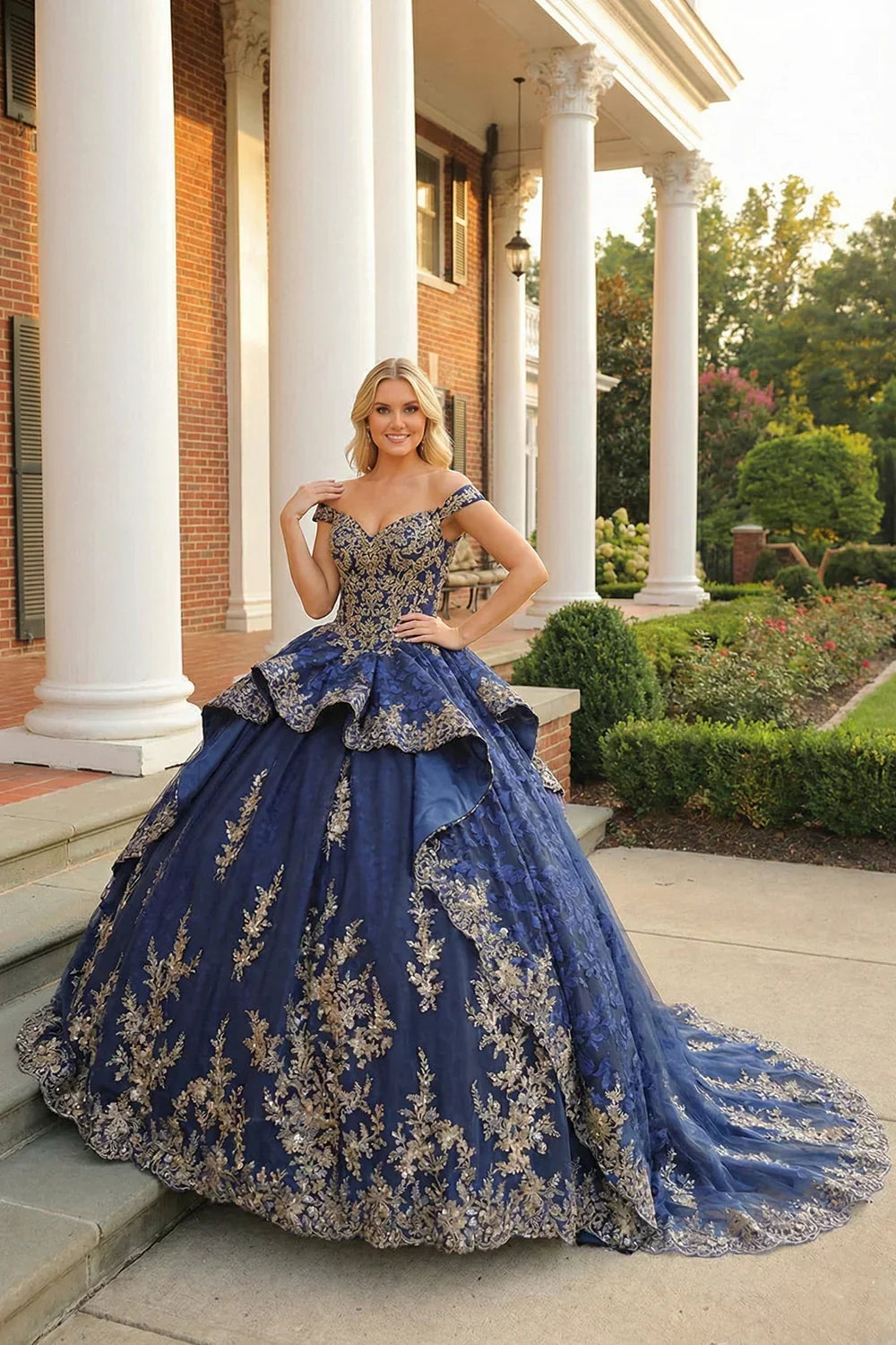 Woman in a blue layered ruffled ball gown with gold floral embroidery and off-shoulder sleeves, posing outdoors.
