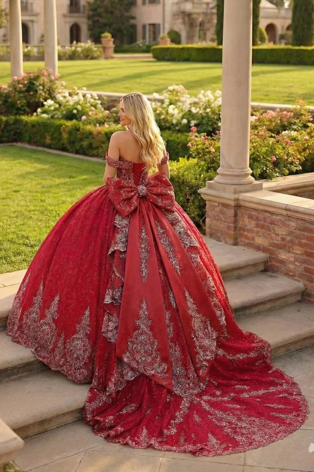 Woman in a red ball gown with silver embroidery and large bow standing outdoors on steps