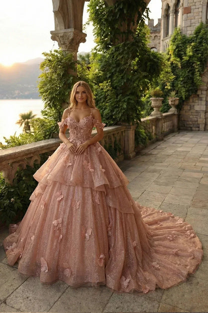Woman in blush pink ball gown with floral appliques and layered tulle skirt on a terrace at sunset