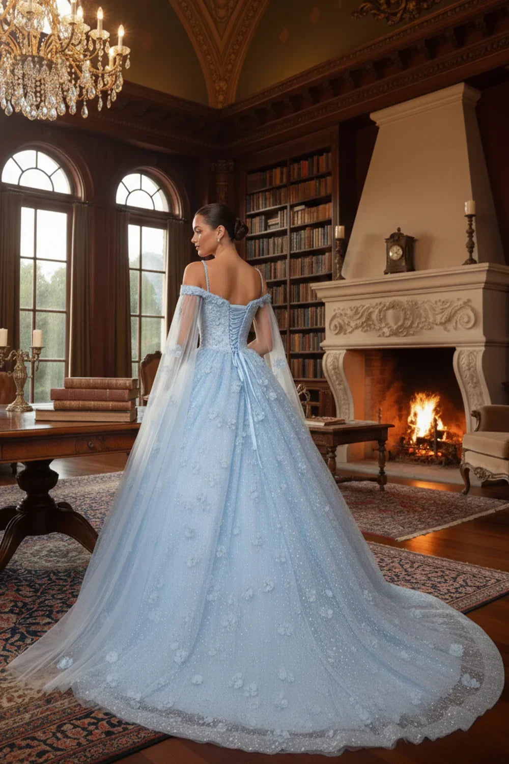 Woman in a light blue off-the-shoulder ball gown with sheer cape and 3D floral details in an elegant library setting.