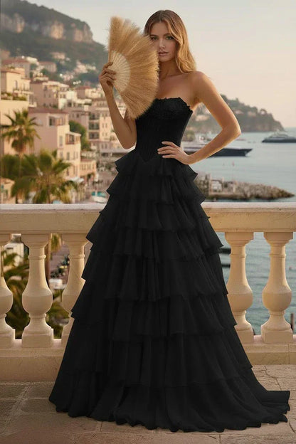 Woman in strapless black tiered ruffle corset prom dress posing on a balcony with ocean view