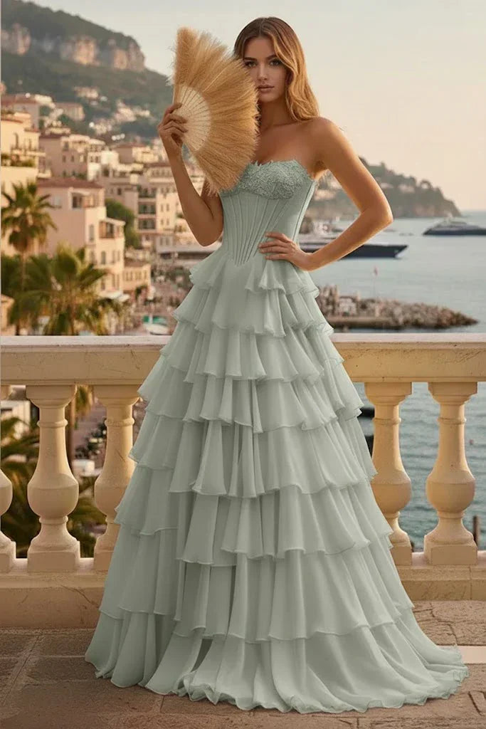 Woman in light blue tiered ruffle corset A-line prom dress with lace-up back, standing on a terrace overlooking the sea.