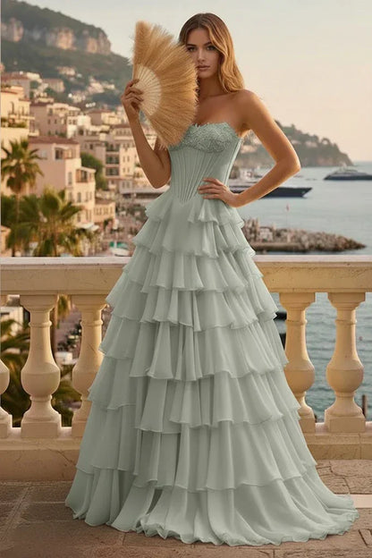 Woman in light blue tiered ruffle corset A-line prom dress with lace-up back, standing on a terrace overlooking the sea.