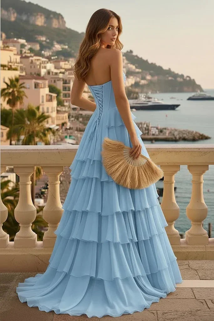 Woman in light blue tiered ruffle corset prom dress with lace-up back on a balcony by the sea