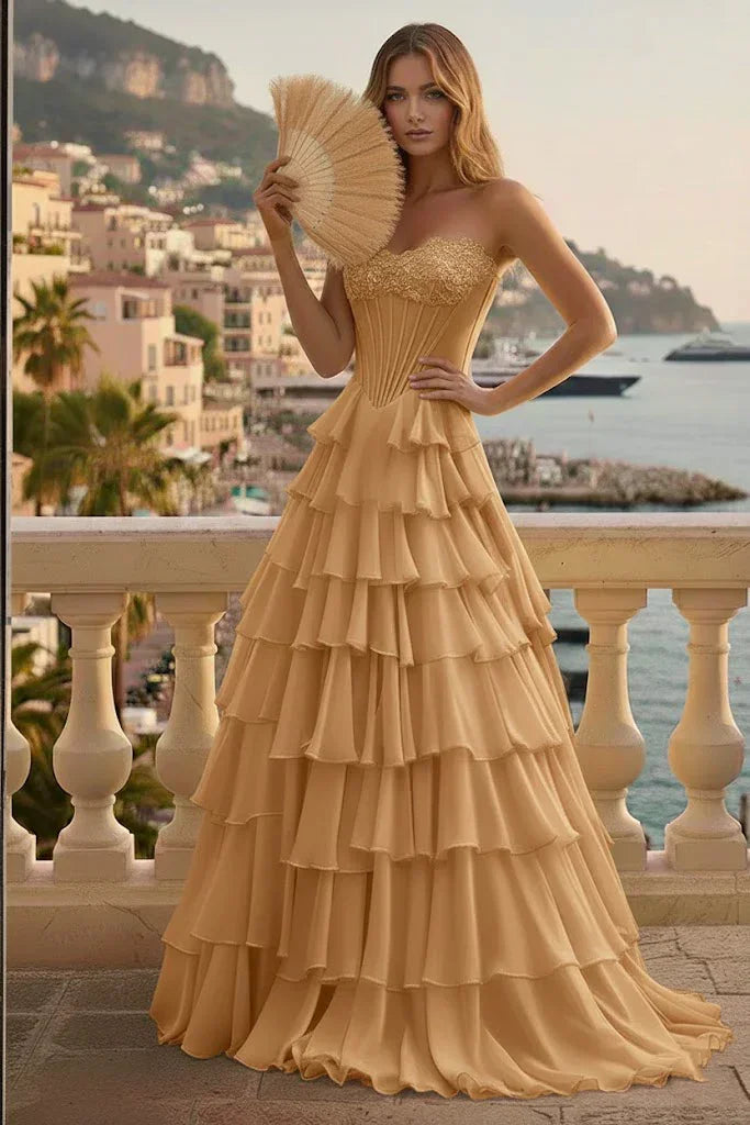 Woman in gold tiered ruffle corset prom dress with lace-up back, posing on a scenic terrace.
